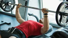 Muž cvičí bench press s činkou v posilovně, trénink horní části těla